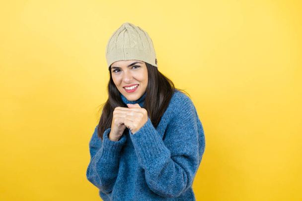 Young beautiful woman wearing blue casual sweater and wool hat Punching fist to fight, aggressive and angry attack, threat and violence - Photo, Image