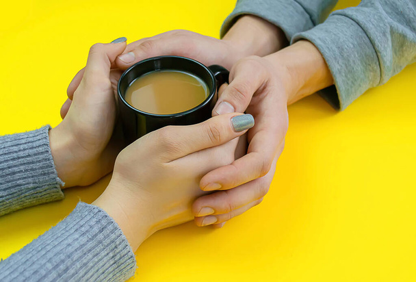 Χέρια σε κίτρινο φόντο με καφέ, αγάπη. Καφέ με γάλα, μαύρο φλιτζάνι. Επιλεκτική εστίαση. - Φωτογραφία, εικόνα