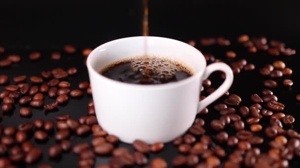Koffie stroomt in witte beker en geroosterde bonen op zwarte achtergrond - Video