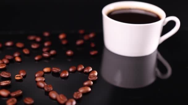 Biały kubek kawy i kształt serca palona fasola na czarnym tle - Materiał filmowy, wideo