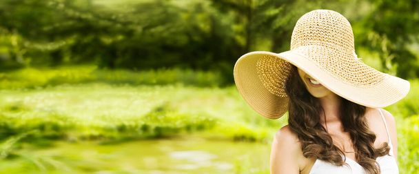 Smiling young woman in sun hat covering her eyes against background of summer green park. Beautiful healthy happy girl enjoying freedom outside in nature. Wide screen banner. - Foto, Imagem