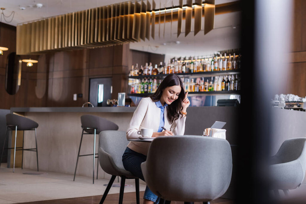 cheerful freelancer showing idea gesture while working in restaurant, blurred foreground - Fotografie, Obrázek