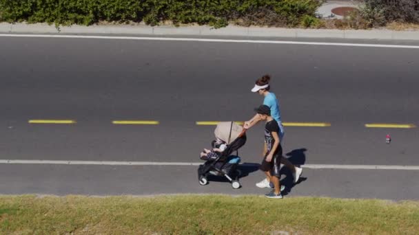 Мать с детьми и детская коляска идет по улице вдоль дороги. - Кадры, видео
