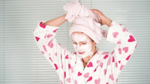Divertente felice donna attraente applicare la crema per la cura della pelle sul viso guardare nello specchio del bagno, sana giovane donna avvolgere asciugamano sulla testa - Filmati, video