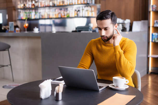 Arabo freelance utilizzando laptop vicino a tazza di cappuccino nel ristorante  - Foto, immagini
