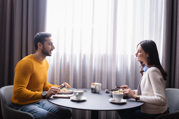 Alegre pareja interracial mirándose mientras cenan en el restaurante  - Foto, imagen