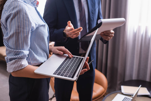Обрезанный вид бизнесвумен с помощью ноутбука рядом с партнером с буфером обмена на размытом фоне  - Фото, изображение