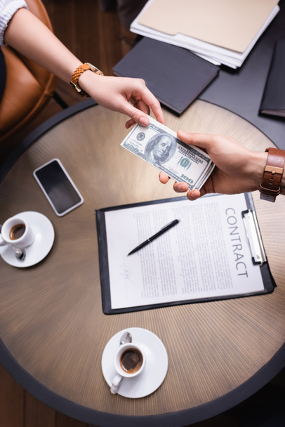 Обрезанный вид бизнесменов, держащих доллары возле контракта и кофе в ресторане  - Фото, изображение