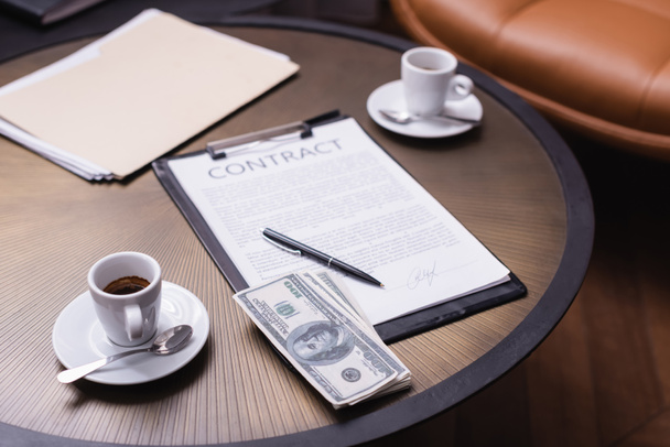 Dollars in de buurt van kopje koffie en contract op wazige achtergrond in restaurant  - Foto, afbeelding