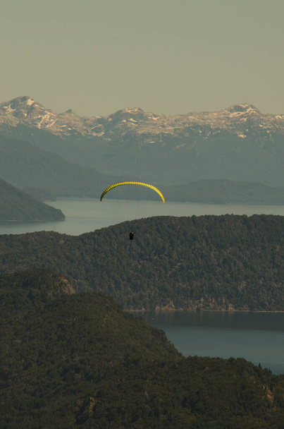 желтый парашютный парашют над городом и окраинами Барилоче, летящий свободно и в одиночестве над озерами и горами, избирательный фокус - Фото, изображение