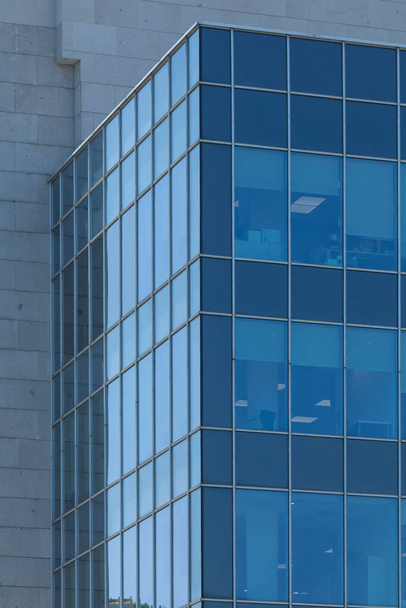 Großaufnahme eines anonymen Bürogebäudes in Madrid, Spanien, unter der sengenden Sommersonne. Ein geschlossener Arbeitsplatz, steril fürs Leben und mit Beton, Stahl und Glas gebaut. - Foto, Bild