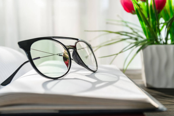 Читання окулярів накладено на відкриті книги над дерев'яним столом біля вікна
 - Фото, зображення