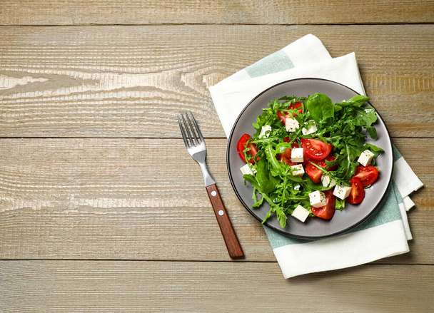Delicious salad with feta cheese, arugula and tomatoes on wooden table, flat lay. Space for text - Foto, Bild