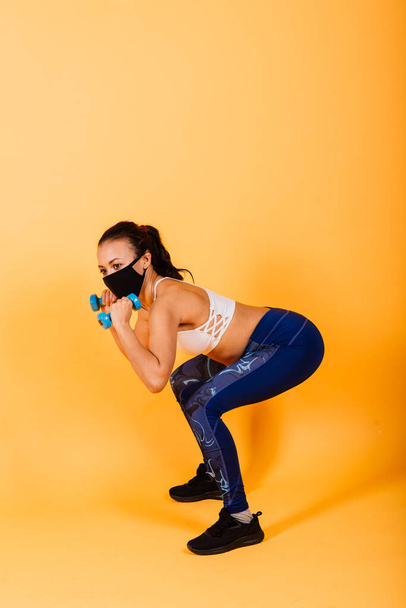 Quarantine is not a hindrance. Dark-skinned sportswoman wearing a medical mask training with dumbbells. Healthcare, fitness and quarantine concept. - Фото, изображение