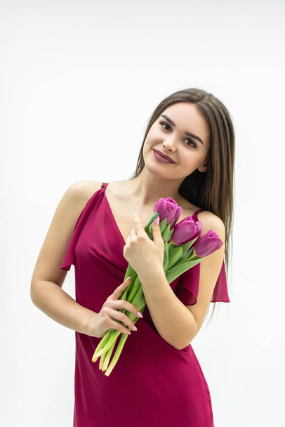 Cute girl with a bouquet of tulips looks with pleasure and smiles tenderly. - Photo, Image