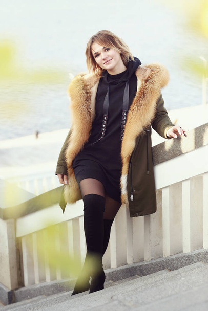  blond business woman in fox fir dawn jacket with hood closeup photo on city park background - Foto, imagen