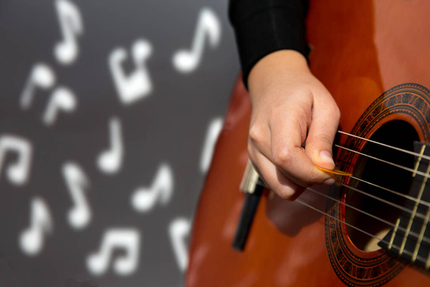 νεαρή γυναίκα παίζει κλασική κιθάρα και μουσικές νότες στο παρασκήνιο. έννοια δημιουργικότητας - Φωτογραφία, εικόνα