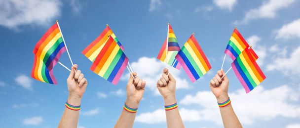 handen met gay trots regenboog vlaggen en polsbandje - Foto, afbeelding