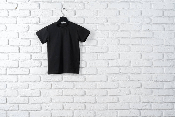 Black t-shirt hanging on a hanger against brick wall - Fotó, kép