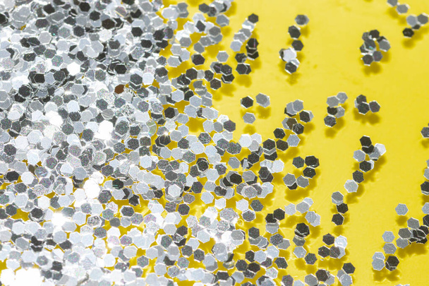 transparante vloeistof met zilverkleurige glitter die over een pastelgele achtergrond stroomt - Foto, afbeelding