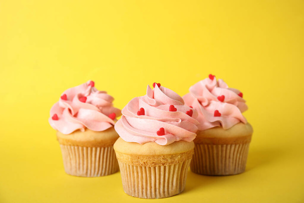 Tasty cupcakes with heart shaped sprinkles on yellow background. Valentine's Day celebration - Zdjęcie, obraz