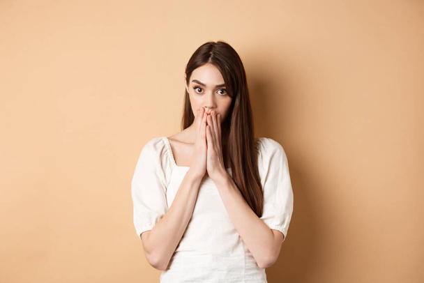 Omg shocking. Speechless woman covering mouth with hands and staring shocked at camera, gossiping, hear stunning news, beige background - Photo, Image