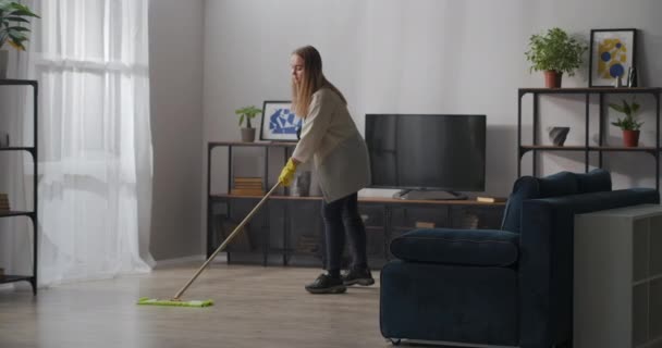 dona de casa está lavando o chão na sala de estar por esfregona, usando luvas de borracha para proteger as mãos, limpeza - Filmagem, Vídeo