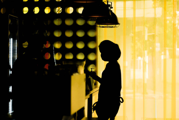 Een silhouet van een vrouw met een masker tijdens het winkelen voor koffie in een coffeeshop, op afstand van anderen tijdens de coronavirus uitbraak. - Foto, afbeelding