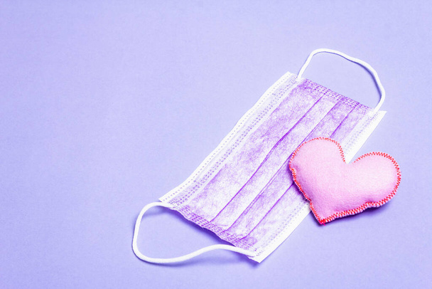 Lilac heart with medical protection mask on light purple background. Concept of healthcare, self-defense - Photo, Image