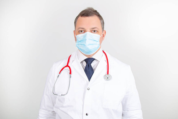 Médico en bata blanca y máscara con estetoscopio con diferentes gestos de pie recto - Foto, Imagen