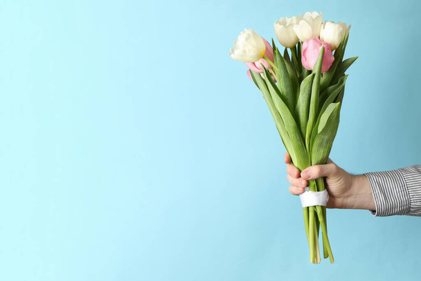 Male hand holds bouquet of tulips on blue background - Photo, image