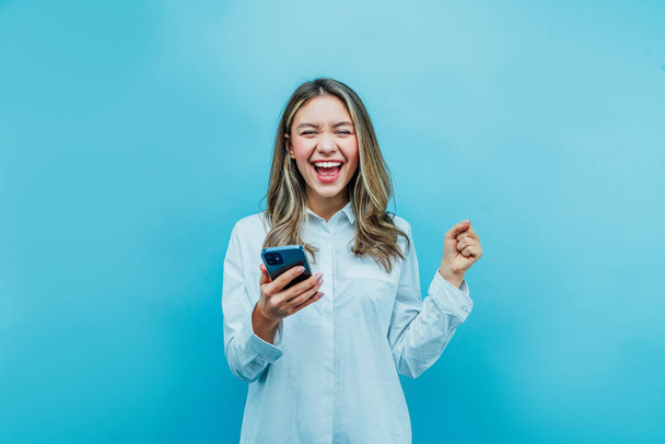 On a blue background joyful girl with a phone in her hands, she is sincerely smiling. Online shopping. Internet-shop. Place for text. Background. - Foto, imagen