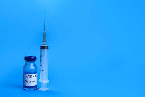 coronavirusvaccin en een spuit op een blauwe achtergrond. Het concept van de strijd tegen de gemoederen - Foto, afbeelding