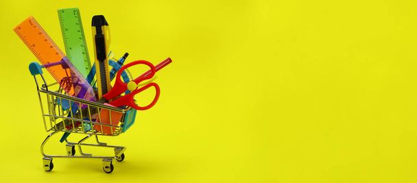 Shopping cart with stationery, school supplies on yellow background - Photo, Image