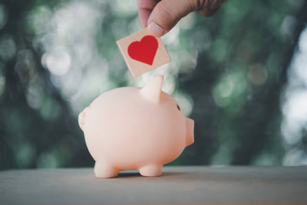Hand put wooden block heart in pink piggy bank. Concept of Insurance for your health - Photo, Image