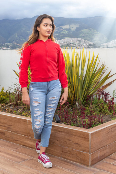 Menina adolescente vestindo jeans, camisola vermelha sapatos esportivos posando em um jardim - Foto, Imagem