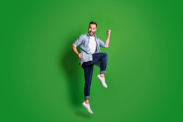 Full size profile photo of impressed funny guy jump wear blue shirt jeans footwear isolated on green color background - Фото, изображение