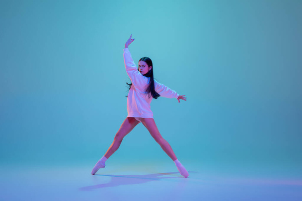 Jovem e graciosa dançarina de balé isolado em fundo estúdio azul em luz de néon. Arte, movimento, ação, flexibilidade, conceito de inspiração. - Foto, Imagem