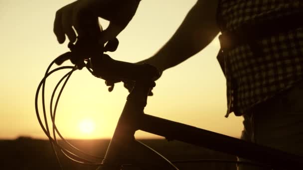 Radfahrer hält Fahrradlenker in der Sonne und rastet im Park aus. Ein Tourist steht auf einem Hügel neben einem Fahrrad und genießt die Natur und die Sonne. Der Reisende reist bei Sonnenuntergang mit dem Fahrrad. Abenteuerkonzept - Filmmaterial, Video