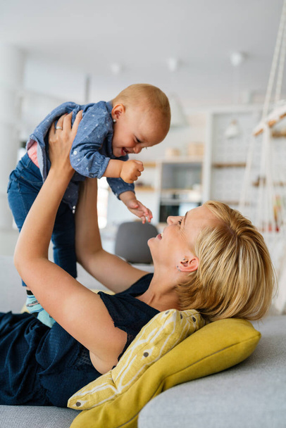 Young beautiful mother playing with her baby girl at home. Family, love concept - 写真・画像