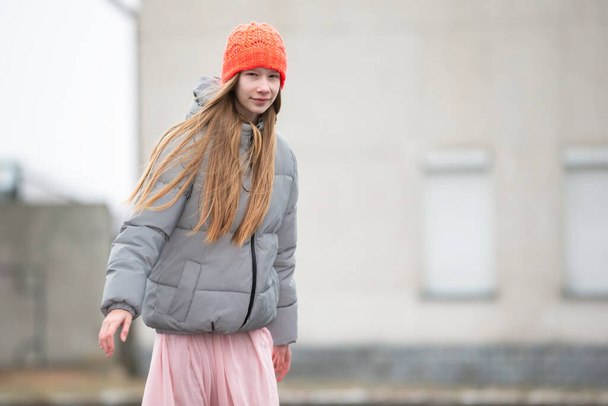 Tienermeisje met gebreide muts en warme jas tegen de achtergrond van de stad. - Foto, afbeelding