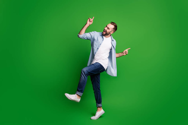 Full size profile photo of optimistic guy dancing wear blue shirt jeans footwear isolated on green color background - Fotó, kép