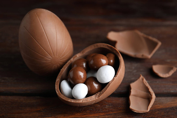 Whole and broken chocolate eggs with candies on wooden table - Fotografie, Obrázek