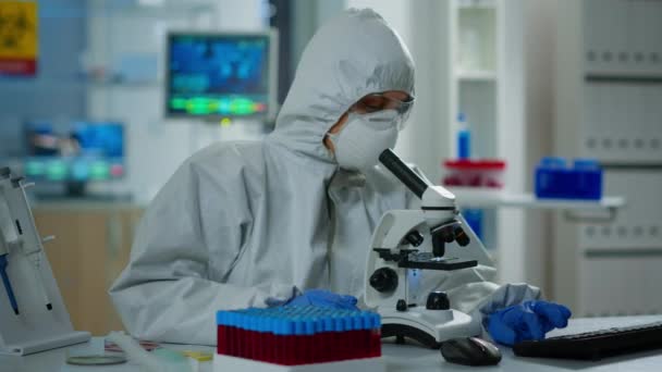 Γυναίκα επιστήμονας σε κοστούμι Ppe εργασίας στο εργαστήριο χρησιμοποιώντας σύγχρονο μικροσκόπιο - Πλάνα, βίντεο