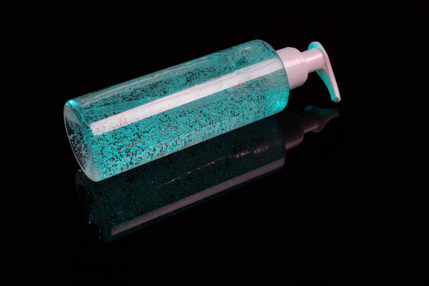 Cosmetic product for makeup remove. Cyan liquid with small air bubbles. Bottle with dispenser. On dark surface background. - Photo, Image