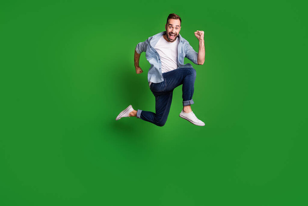 Full size profile photo of optimistic funky guy jump wear blue shirt jeans footwear isolated on green color background - Фото, изображение