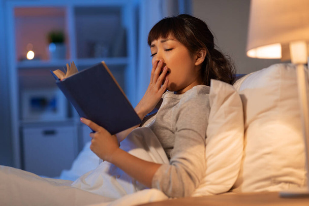 tired asian woman reading book in bed at home - Photo, Image