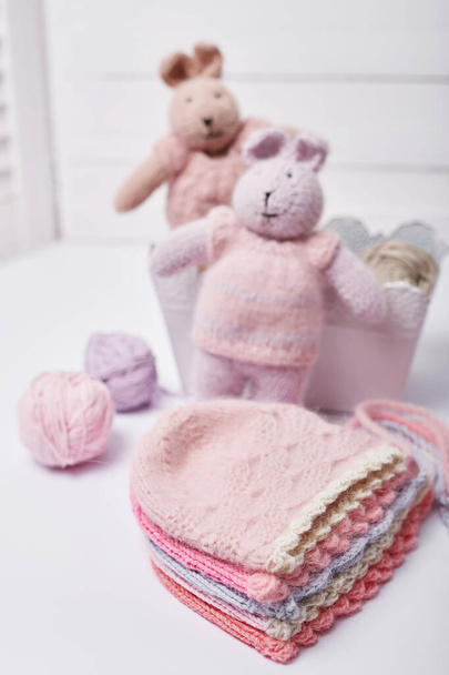 Needlework and knitting. Hobbies and creativity. Knit for children. Knitted toys rabbit and hat. Handmade toy hare. Baby cap. Yarn, threads and balls. - Fotó, kép