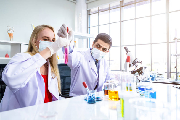 Two scientists are working holding looking at test tube with sample in a chemistry lab scientist or young female and male researcher are doing investigations in Laboratory analysis background - Valokuva, kuva