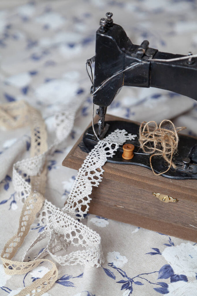 Vintage manual sewing machine and a skein of thread on a white fabric background with a blue pattern close-u - Φωτογραφία, εικόνα